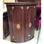 A George III mahogany wall hanging corner cupboard, of bow fronted form, the doors inlaid with