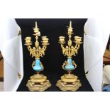 A pair of gilt clock garnitures with porcelain centres on wooden gilt stands