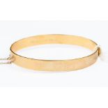 A 9ct gold bangle, hinged with engraved leaf decoration, width approx. 7mm, internal diameter