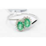 An emerald and white zircon 10ct white gold double cluster cross over ring, the claw set oval