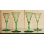 A set of four early 19th Century green glass sherry glasses, trumpet shaped with faceted bowls and