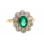 An emerald and diamond cluster 18ct gold ring, the oval rub over set emerald weighing approx. 1.