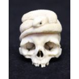 A Japanese ivory netsuke, Meiji period, modelled as a skull with a serpent curled on the top, 3cm.