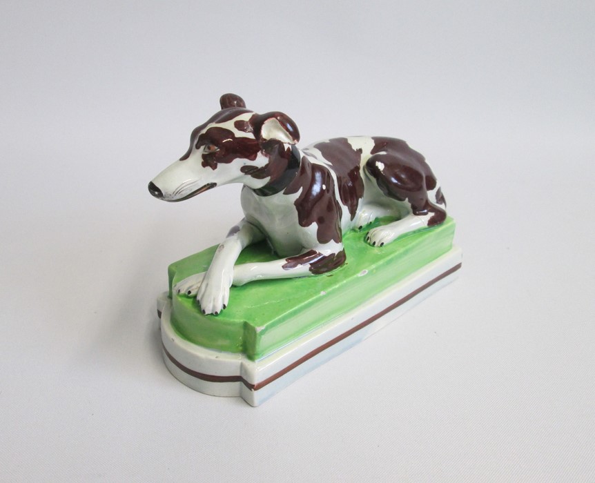 A Staffordshire model of a recumbent Greyhound/Whippet painted with brown markings, laying on a