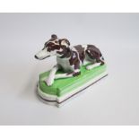 A Staffordshire model of a recumbent Greyhound/Whippet painted with brown markings, laying on a