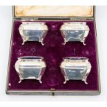 A set of four Edwardian silver salts, cellarette shaped on four scroll feet, blue glass liners, by