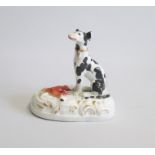 A Staffordshire Model of a Seated Hound painted with black markings with a Hare at its feet. Sitting