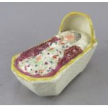 An early nineteenth century Staffordshire pearlware figure of a sleeping baby in a rocking cradle,