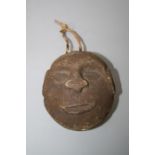 A primitive carved stone head with broad nose and pronounced brow, the head with a vine suspension