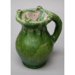 A green glazed pottery puzzle mug/jug with pierced neck and baluster body and hollow loop handle.