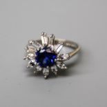 A synthetic sapphire and clear stone cluster ring, the circular cut sapphire in six claw mounts,