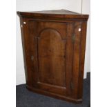 A late 18th century oak wall mounting corner cupboard, the arch fielded panel door enclosing