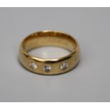 A three stone diamond ring, the brilliant cut diamonds flush mounted into a wide 18ct gold band,