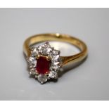 A ruby and diamond cluster ring, the step cut, cut cornered ruby in four claw mount above a border
