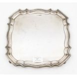 A George V silver shaped square salver with raised border on four scroll feet, by Walker & Hall,