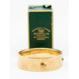 A 9ct gold bangle having engraved decoration to the front and plain on the back with safety chain,