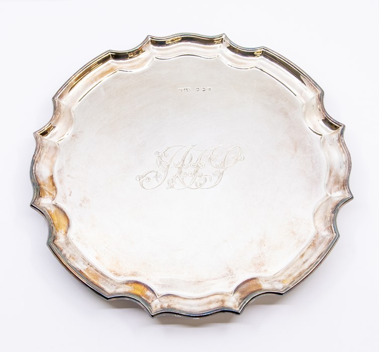 A Georgian style plain circular salver with pie crust rim, on three scroll feet, the centre engraved