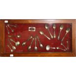 A cased wall display of mostly 19th silver spoons and other items including caddy spoons , enamel