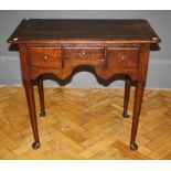 An 18th century oak lowboy, the planked top over a shaped apron and three drawers with brass