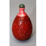 A Chinese cinnabar lacquer snuff bottle with lotus decoration and jade coloured stopper. 8 cms.