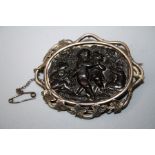 A Victorian jet brooch with silver "ivy" mount. The jet panel carved with cavorting cherubs. Bearing