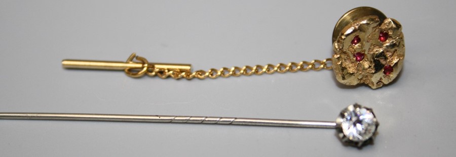 A tie pin fashioned as a gold nugget set with ruby coloured stones together with a paste set stock