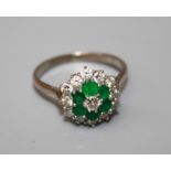 An emerald and diamond cluster ring, the principal brilliant cut diamond within a border of five