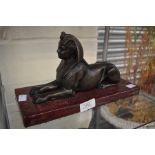 A base metal sculpture of a Sphinx on a marble effect base