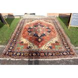A large woollen hand knotted room size rug, of symmetrical design with geometric patterns on a red