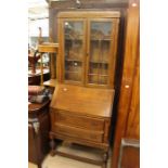 A 1940's oak bureau bookcase, the upper section with two doors enclosing shelves, the base section