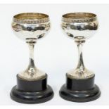 A pair of early 20th Century plain silver coupe style goblets, with band of floral decoration to rim