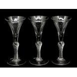 A set of three George III hand blown wine glasses, each having a trumpet shaped bowl and raised on