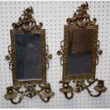 A pair of brass girondole wall mirrors, each with cherub and trophy cast frame with twin scrolled