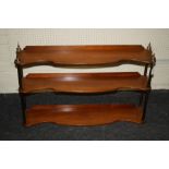 An Edwardian mahogany set of three tier serpentine fronted hanging wall shelves with brass