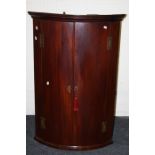 An early 19th century mahogany barrel fronted hanging corner cupboard. 113 x 74 cms.