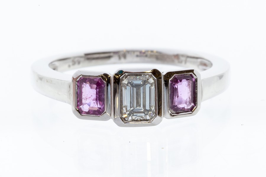 A pink sapphire and diamond three stone 18ct white gold ring, comprising a central emerald cut