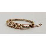 An antique precious yellow metal and cultured pearl set floral hinged bangle, the front having