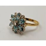 An 18ct. gold, light blue stone and diamond cluster ring. set central round brilliant cut diamond