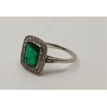 An Art Deco style precious white metal, diamond and emerald ring, having emerald cut emerald to