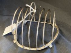 White Metal: Oval wire toast rack, tests as silver, stood on four feet NB: One engraved with th Hood