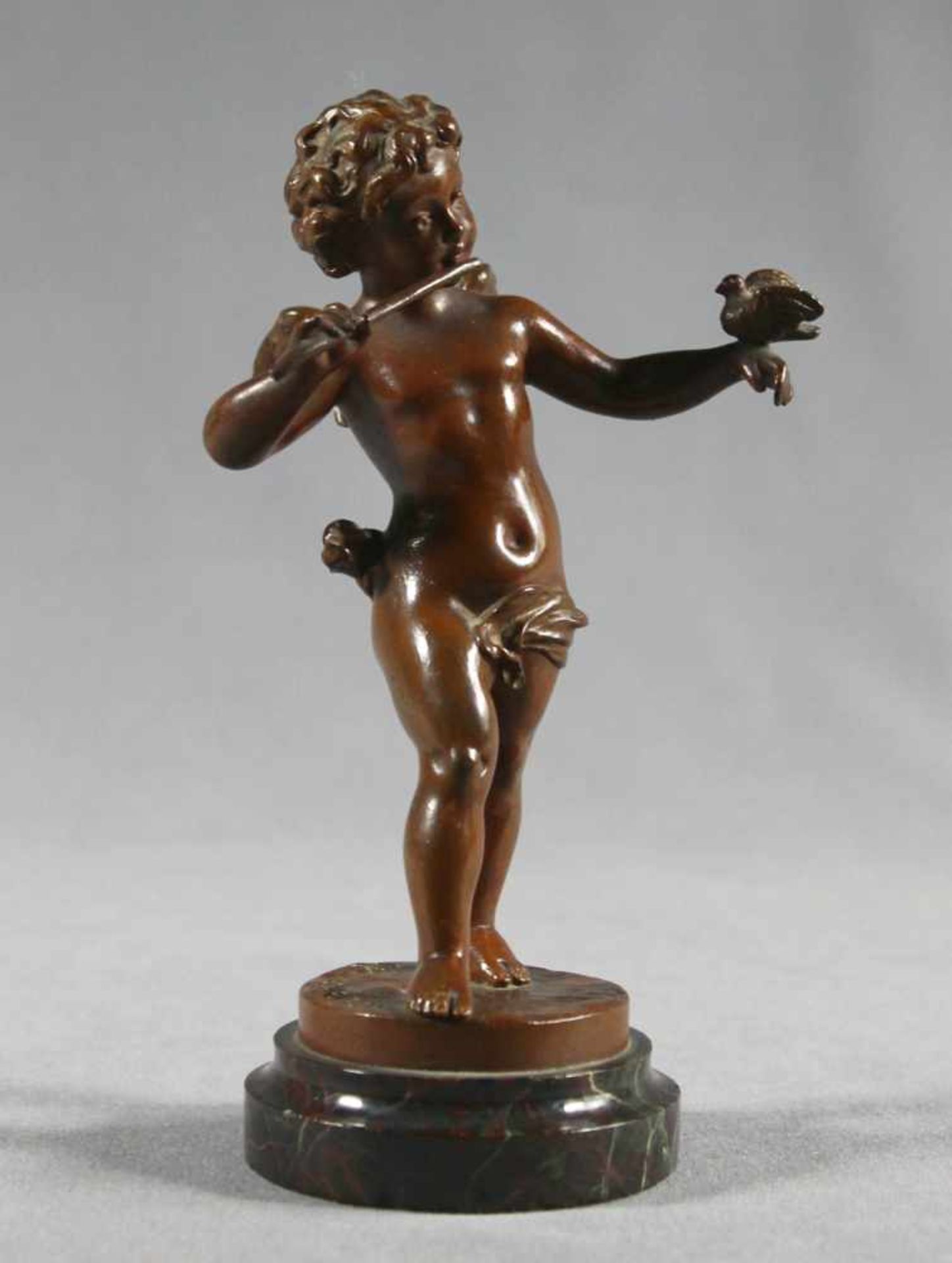 1 kleine Bronzefigur "Putto", auf rundem Marmorsockel "Musizierender Putto mit Vogel auf der