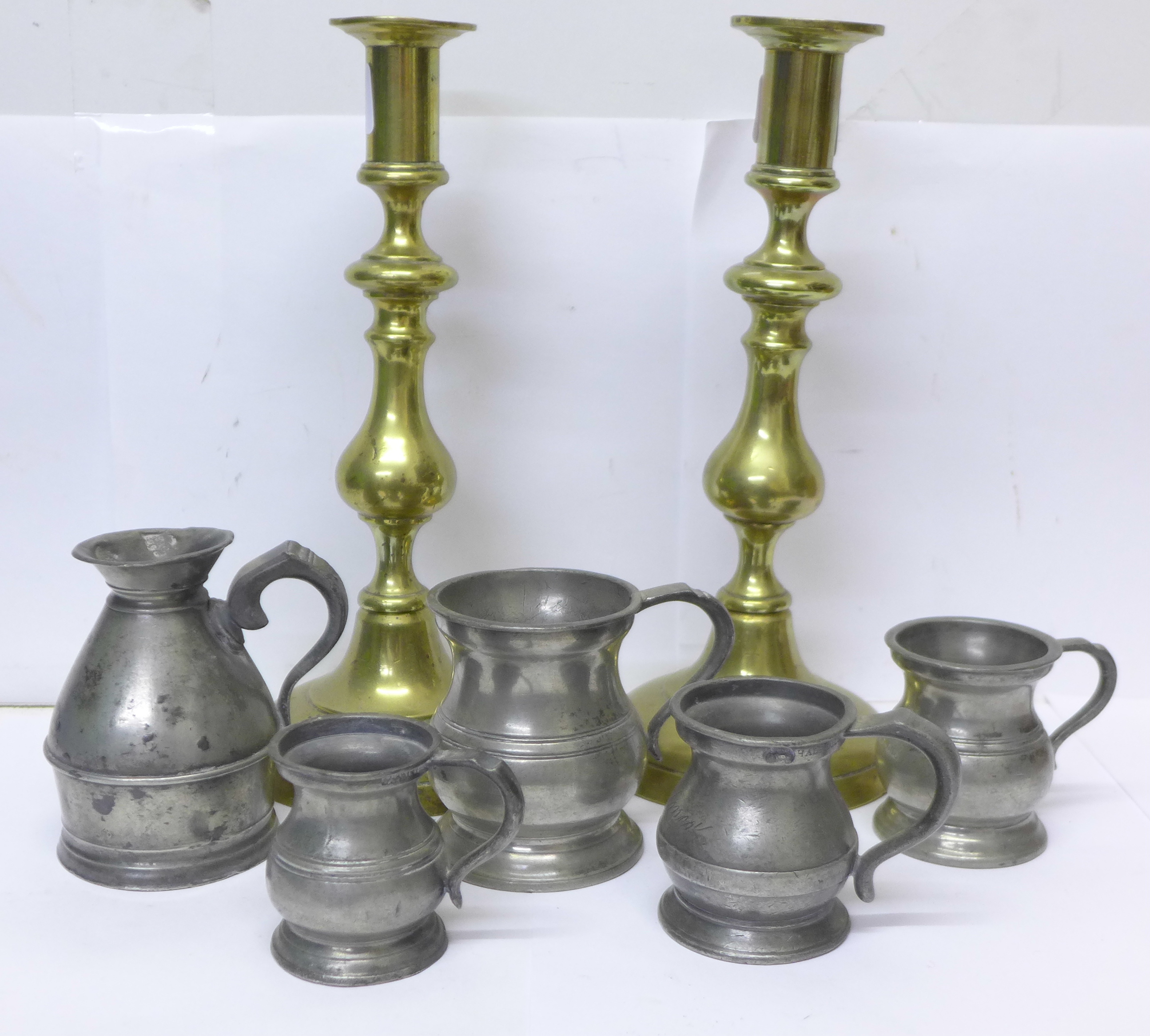 A pair of brass candlesticks, four measures and a 1 noggin measure in the form of a milk churn