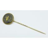 A yellow metal set stick pin decorated with an image of a Japanese gentleman with fan and sword,