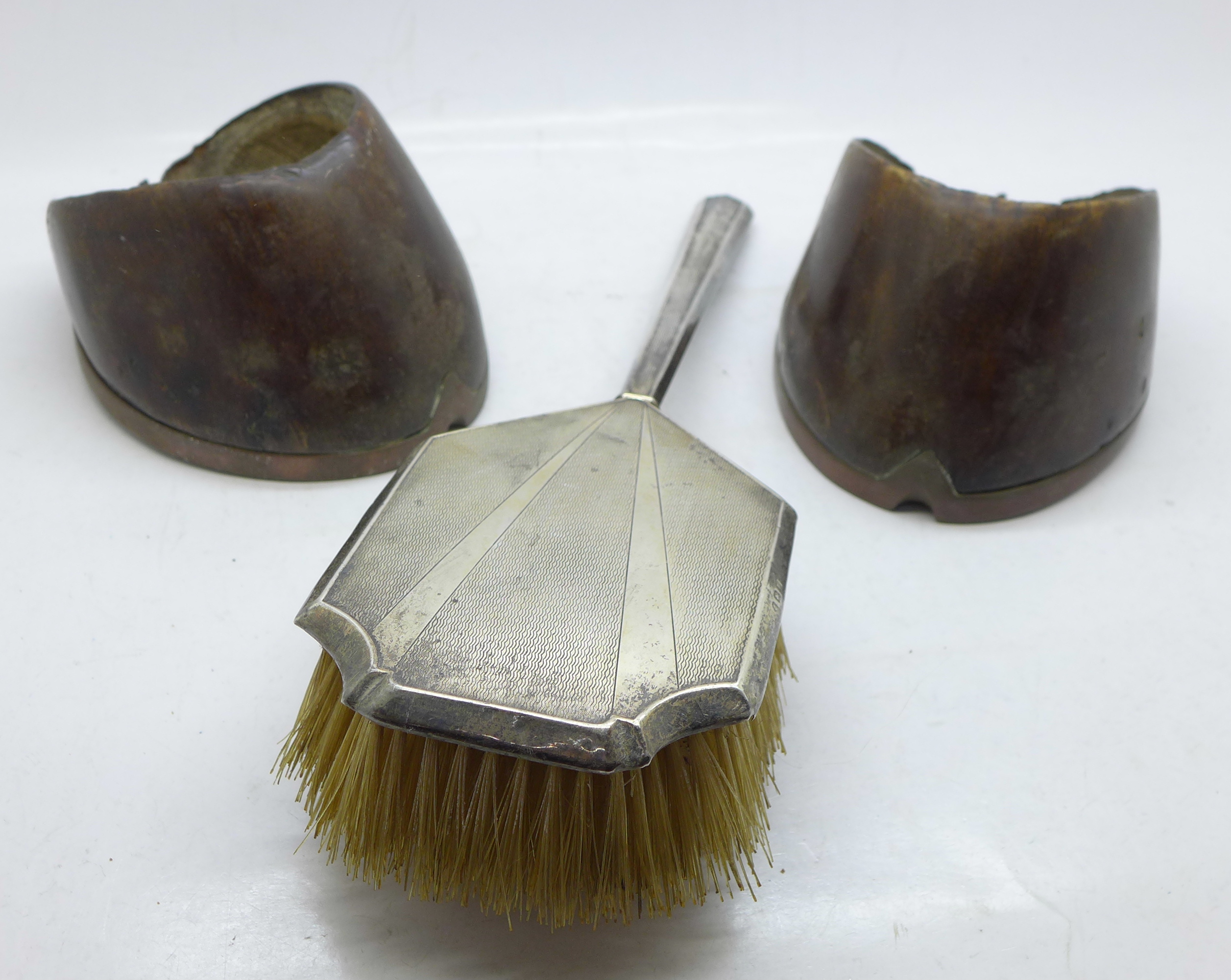Two horse's hoofs with copper shoes and a silver hair brush