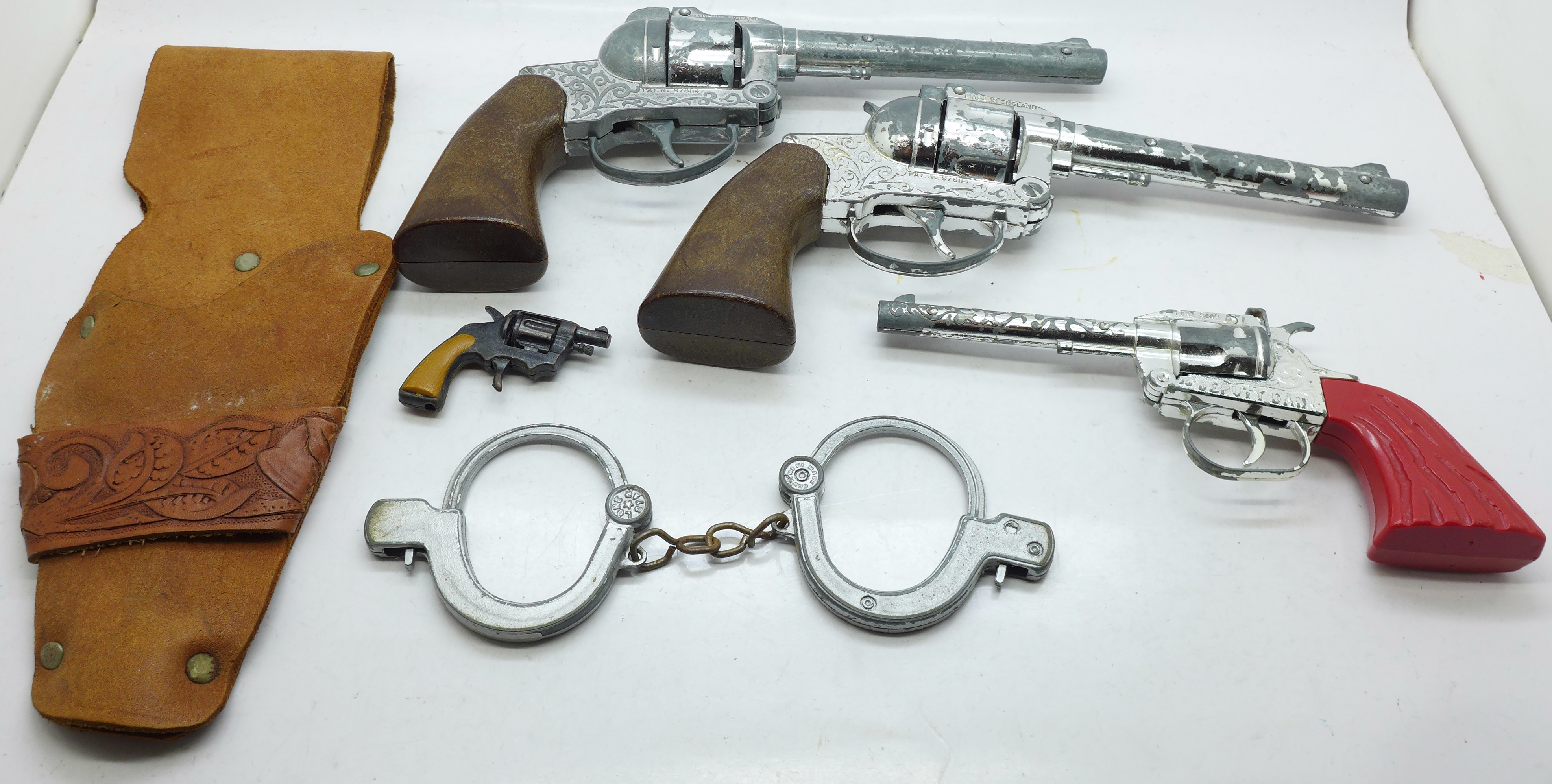 Three cap guns, Lone Star and Crescent Toys, a pair of toy handcuffs and a holster