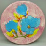 A Moorcroft plate decorated with blue flowers on a pink ground, marked cc89, 26cm