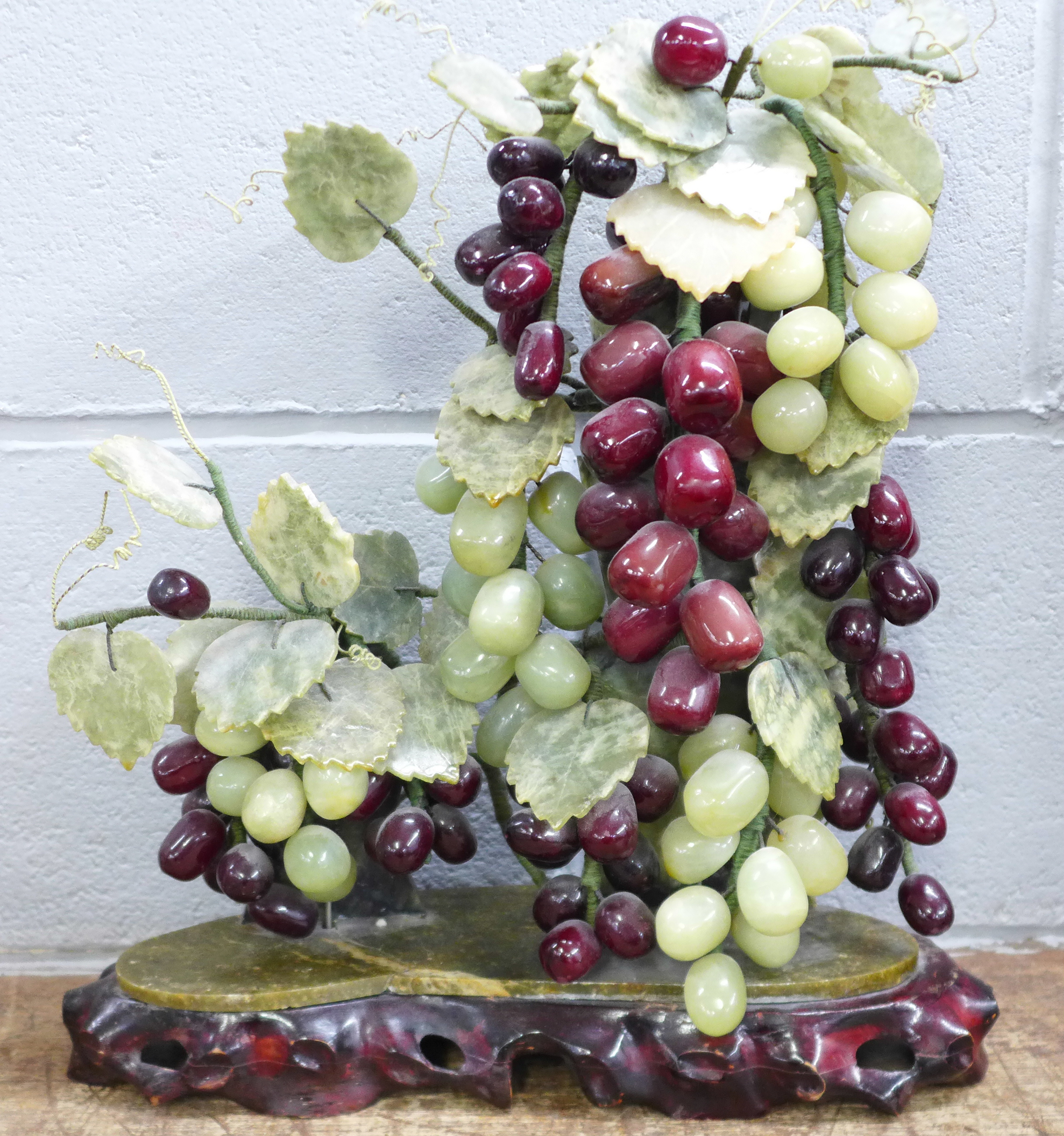 An Asian art centrepiece, jade grapes and carved soapstone vine leaves with carved wooden base, 39cm