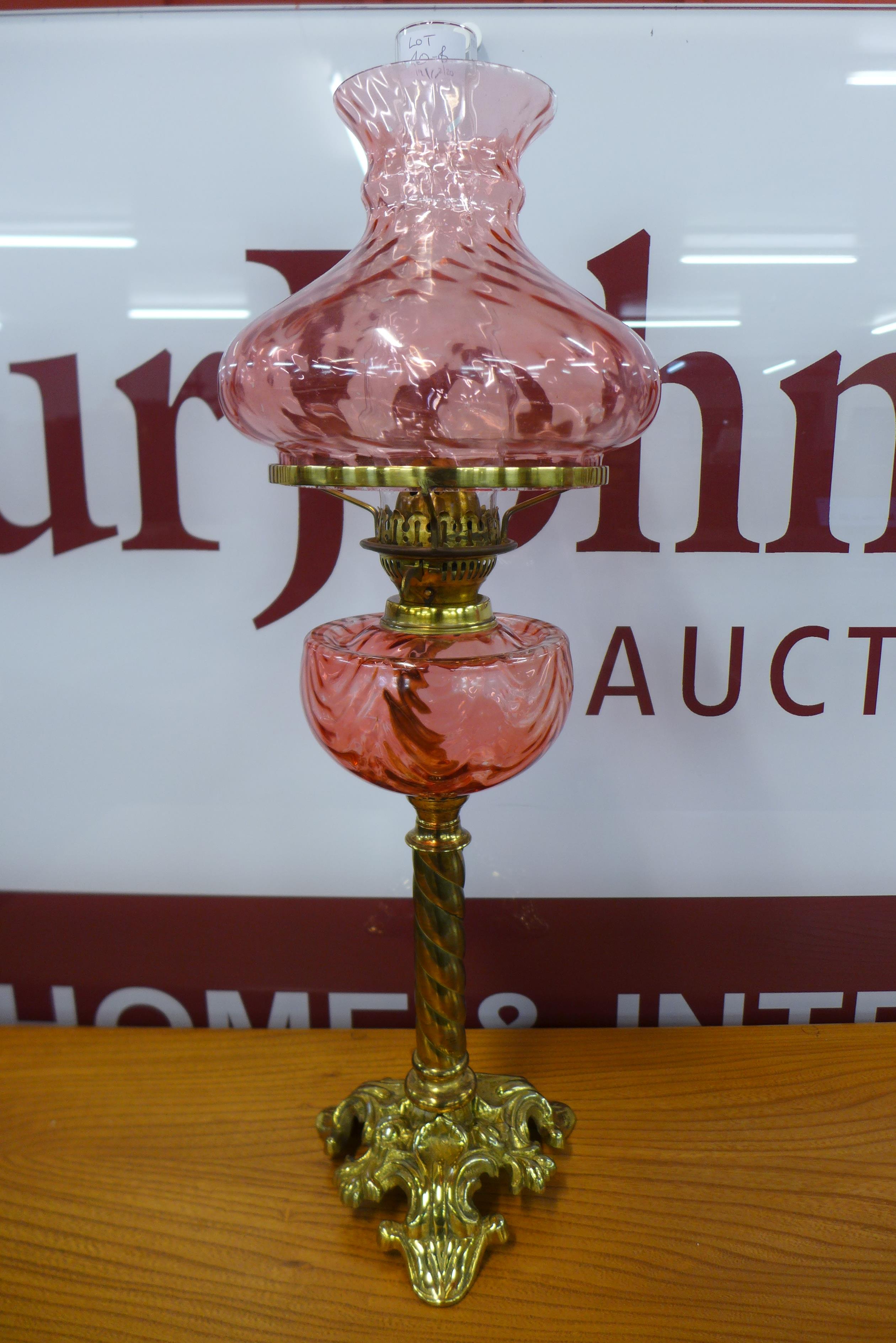 A Victorian brass oil lamp, with cranberry glass reservoir and shade