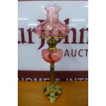 A Victorian brass oil lamp, with cranberry glass reservoir and shade