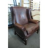A large oversized mahogany and brown leather wingback armchair